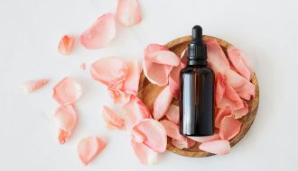 Top view of empty brown bottle for skin care product placed on wooden plate with fresh pink rose petals on white background isolated