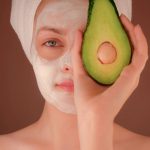 woman with white face mask holding green fruit